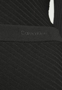 Tissu noir côtelé avec des motifs diagonaux, doté d'une large ceinture élastique avec "Calvin Klein" subtilement embossé.