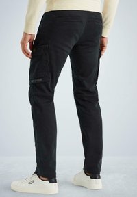 Schwarze Cargo-Hosen mit mehreren Taschen, strapazierfähigem Stoff, gerader Beinform und dezentem Logo-Detail. Getragen mit weißen Sneakers.