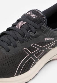 Zapato de correr ASICS negro con acentos en rosa, etiqueta impermeable Gore-Tex, entresuela Amplifoam y parte frontal bien ajustada.