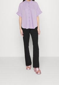 Levandulová košile na knoflíky s krátkými ohrnutými rukávy, v kombinaci se štíhlými černými kalhotami a lesklými růžovými sandály na blokovém podpatku.