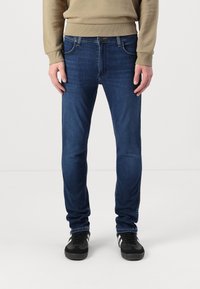 Temno modre jeans hlače slim fit kroja, z sprednjimi žepi in subtilnimi šivi, v kombinaciji z črnimi supergami.