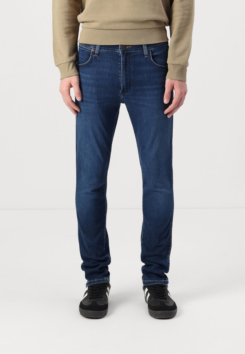 Temno modre jeans hlače slim fit kroja, z sprednjimi žepi in subtilnimi šivi, v kombinaciji z črnimi supergami.