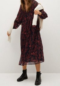 Floral-patterned, long-sleeve dress in navy with red designs, featuring a gathered neckline and a flowing silhouette, paired with chunky black boots.