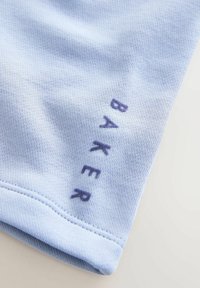 Material sportiv de culoare albastru deschis, cu țesătură texturată, prezintă text brodat albastru închis „BAKER” aproape de marginea cusută.