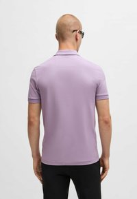 Polo shirt in light purple, short sleeves, smooth texture, subtle collar, tailored fit, worn with black pants, viewed from the back.
