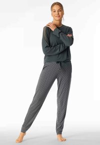 Long-sleeve dark green top with sheer shoulder accents, paired with patterned gray pants featuring a drawstring waist and tapered cuffs.