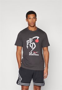 Sort bomulds T-shirt med et hvidt og rødt basketballgrafik. Sammen med mørke shorts med hvide detaljer og perforeret tekstur.