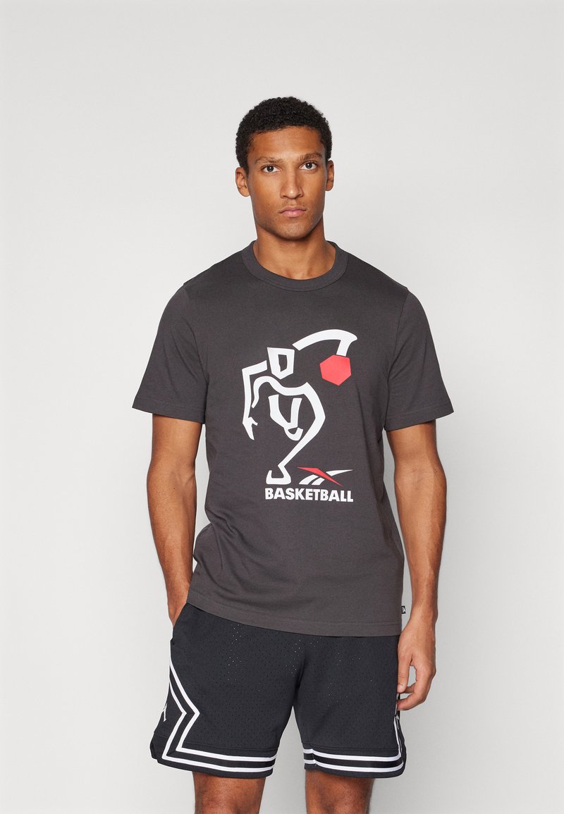Sort bomulds T-shirt med et hvidt og rødt basketballgrafik. Sammen med mørke shorts med hvide detaljer og perforeret tekstur.