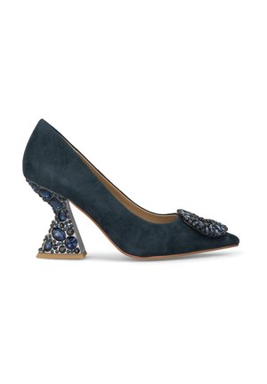 Pump in suede blu scuro con punta affilata, adornato da una spilla gioiello e un tacco geometrico testurizzato con diverse gemme blu.