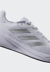 Baskets de sport gris clair avec dessus en mesh, accents argentés, semelle texturée et trois bandes réfléchissantes sur le côté.