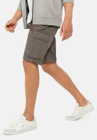 Grå cargo-shorts med flere lommer, parret med hvide sneakers. Stofdet ser let og glat ud.