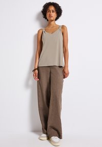 Ljusbeige, ärmlös topp med V-hals och subtila axelaccenter, i kombination med lösa, bruna, linneaktiga byxor och ljusa sneakers.