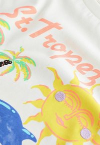 Vit bomullströja med färgglada grafik av palmer, en sol och texten "St. Tropez" i orange och rosa nyanser.