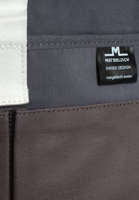 Grauener Stoff mit glatter Textur und kontrastierendem weißen Träger. Enthält ein schwarzes Etikett mit dem Text "Margelisch" und "Schweizer Design".