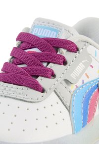 Valkoinen sneaker, jossa on violetit nauhat, vaaleanharmaat yksityiskohdat ja pastellinsiniset, vaaleanpunaiset sekä keltaiset yksityiskohdat. Teksturoidut pinnat, joissa on rei'ityksiä.