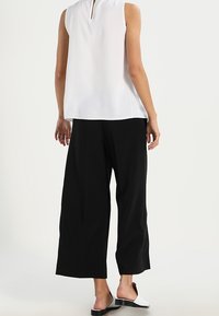 Bílý bezrukávový top s rozparkem na zádech, spárovaný s volnými černými kalhotami culottes a černo-bílými nazouvacími botami. Minimalistický design.