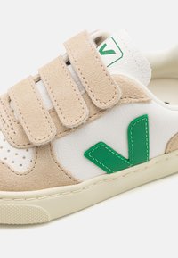Sneaker in suede beige e pelle bianca con tre cinturini in Velcro. Accento in gomma verde con logo sul lato. Suola testurizzata per una migliore aderenza.