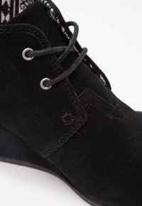 Stivaletto in camoscio nero con tacco a zeppa, design con lacci, dettagli ricamati nella fodera interna e accenti di cucitura a contrasto.