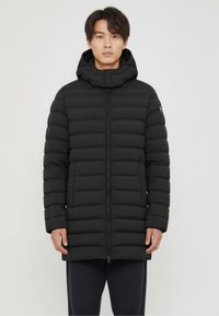 Black puffer jacket with a zip front, a detachable hood, and horizontal quilting. Features two front pockets and a logo on the sleeve.