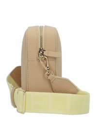 Sac en cuir beige avec une fermeture éclair dorée et des accessoires en métal. Il présente une texture douce et une sangle jaune réglable avec un logo subtil.