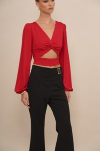 Red long-sleeve top with a twist front and cutout, paired with high-waisted black trousers featuring a rectangular belt buckle.