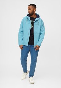 Ljusblå huva jacka med vita dragsko, dragkedjestängning, sidofickor, bärs över en svart t-shirt och blå jeans, kombinerad med vita sneakers.