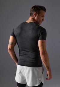 Enganliegendes sportliches T-Shirt mit kurzen Ärmeln in Dunkelgrau, aus strukturiertem Stoff mit Raglanärmeln. Getragen mit hellen Shorts, die ein körperbetontes Design zeigen.