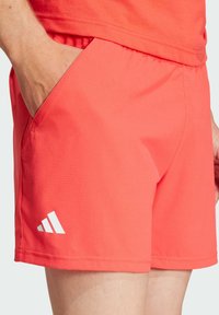 Coral athletic shorts with a textured fabric, featuring side pockets and a white logo accent near the hem.