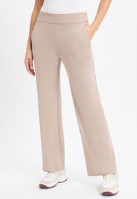 Pantalons beige à taille haute, larges et confortables, en tissu lisse et extensible, avec des poches latérales et un logo sur la ceinture.