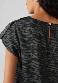 Blusa blu scuro con un motivo testurizzato di linee verticali verde chiaro, scollo rotondo, maniche corte e chiusura con bottone sul retro.