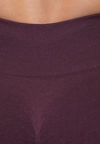 Tejido de punto burdeos con una cinturilla ancha y acanalada. El material es suave, con una textura sutil y un diseño sin costuras cerca del centro.