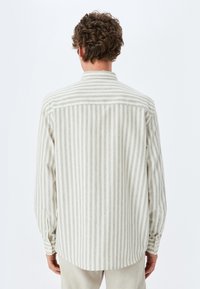 Camisa de hombre de manga larga en beige claro con rayas grises verticales, con cuello estándar y puños abotonados. Tejido suave y texturizado.