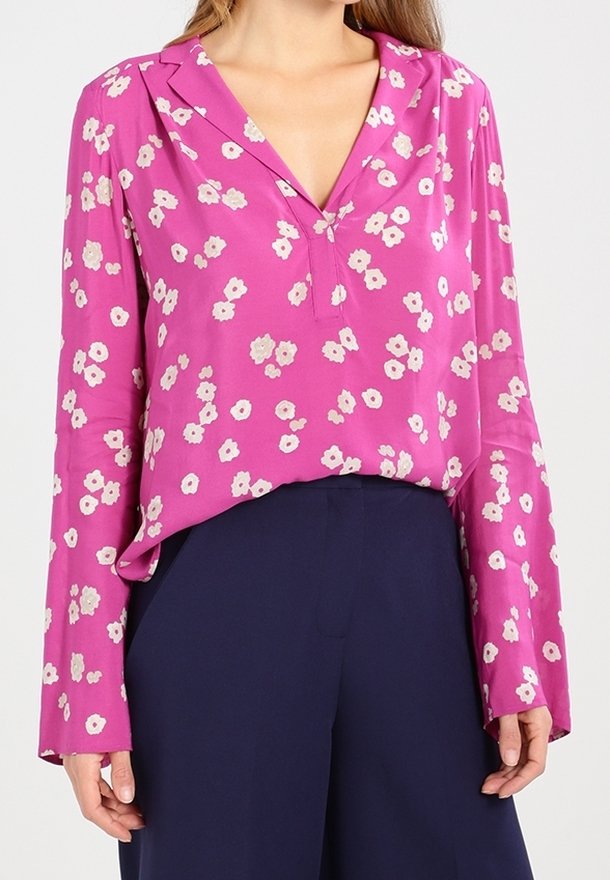 Blouse fleurie rose avec col en V, manches longues et coupe ample. Présente de petits motifs floraux blancs et jaunes sur un tissu lisse.