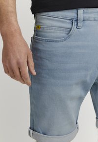 Ljusblå denimshorts med en något bleknad tvätt, upprullade fållar och en gult märkt fickdetalj. Slät yta och klassisk passform.