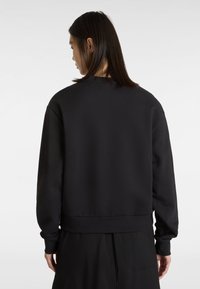 Sweatshirt noir à col rond avec des manches longues, des poignets et un ourlet côtelés, présentant une texture lisse et un design minimaliste.