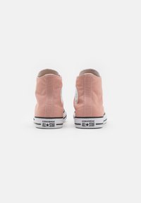 Zapatillas caninas altas rosas de lona con costuras blancas y parche con el logo, con suelas de goma en blanco y negro, vista trasera.