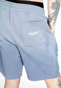 Lyseblå bomuldsshorts med elastisk talje, baglomme med "MULTIPLY APPAREL" logo i hvid og glat tekstur.