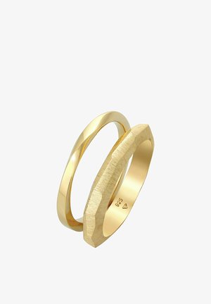 Zwei überlappende Ringe: ein glatter und polierter goldener Band, der andere mit einer strukturierten, matten Oberfläche und geometrischer Form. Beide in Goldfarbe.