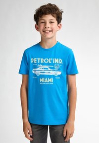 Camiseta de algodón azul con mangas cortas, que presenta un gráfico de un coche retro y el texto "PETROL IND. MIAMI" en blanco y amarillo.