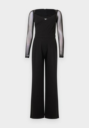 Combinaison noire à manches longues en maille transparente, col carré, taille cintrée et pantalons larges sur un fond uni.