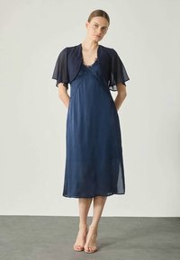 Vestido midi azul marino hecho de una tela ligera, con un detalle de encaje en el corpiño, mangas cortas tipo volantito y una silueta fluida.