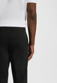 Czarne spodnie z teksturowanej tkaniny, z tylnymi kieszeniami o subtelnych detalach oraz dopasowaną talią, zestawione z białą, teksturowaną koszulą.