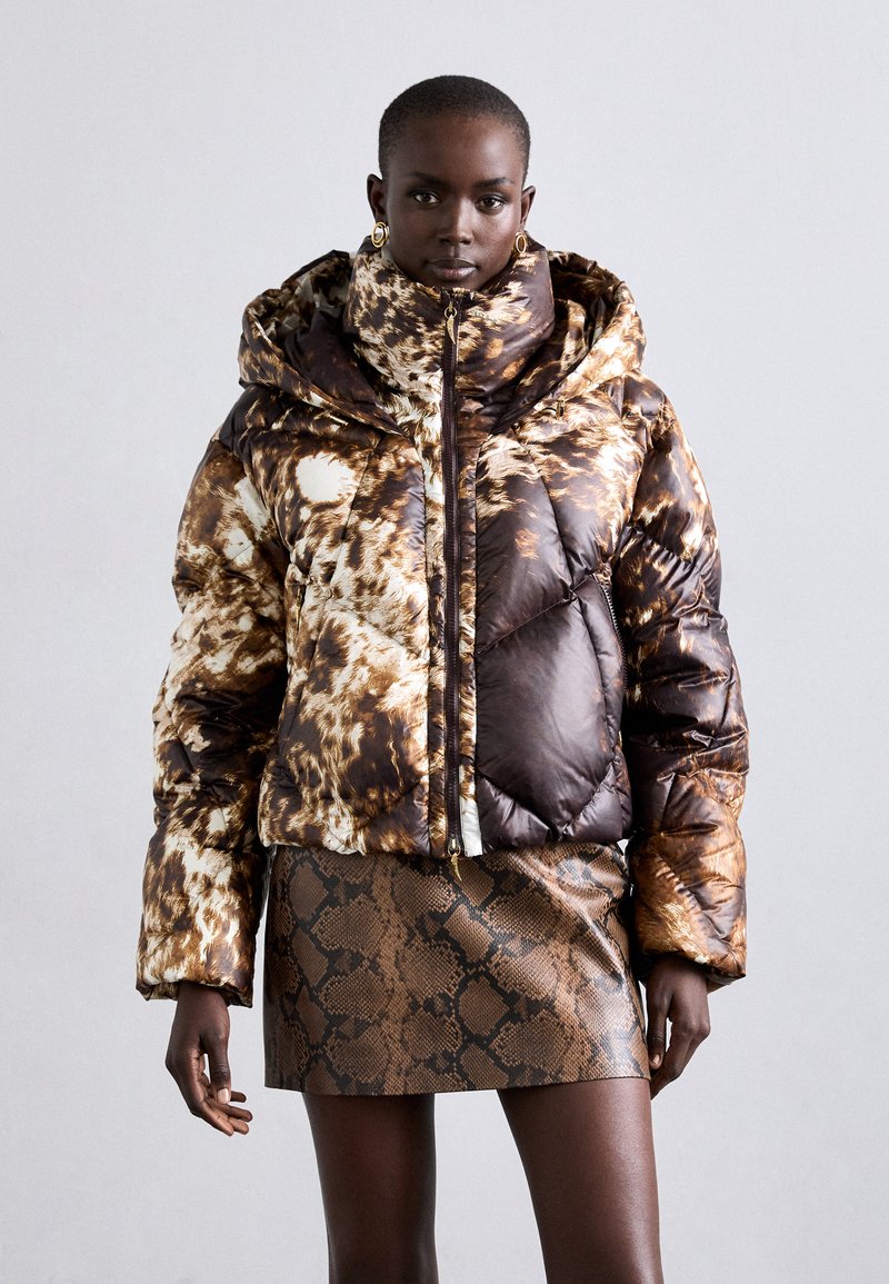 Jachetă puffer cu un model abstract lucios, în nuanțe de brun și crem, având un guler înalt, închidere cu fermoar și un design matlasat. Asortată cu o fustă cu imprimeu de șarpe.