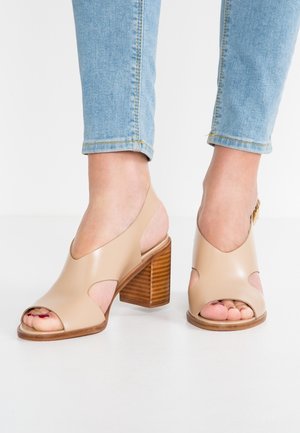 Beige blokhælssandaler med åben tå og udskæringer i siderne, båret med lyseblå jeans.