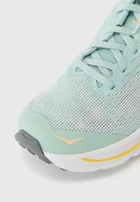 Leichte Laufschuh mit einem mintgrünen Mesh-Obermaterial, grauer Sohle und orangen Akzenten. Verfügt über ein strukturiertes Muster und ein Schnürdesign.