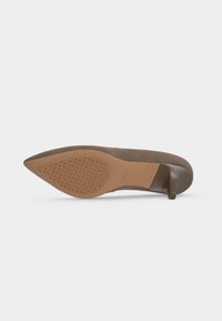 Chaussure à talon haut marron à bout pointu montrée par la semelle avec une semelle texturée et un talon fin sur fond blanc.