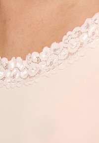 Ljust rosa linne med en scallop-lace halsringning med blommönster och en slät, mjuk textur.