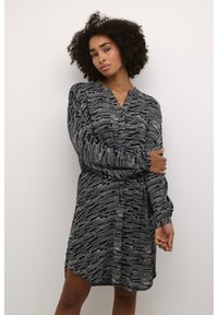 Abito a maniche lunghe in blu navy con un tessuto testurizzato e pattern. Caratterizzato da scollatura a V e bottoni, vita arricciata e spacco laterale.
