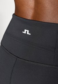 Leggings deportivos negros hechos de una tela elástica. Las características incluyen una textura suave, una cintura alta y un logo blanco en la parte posterior.