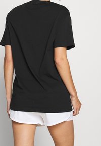 Černé bavlněné tričko s krátkým rukávem, kulatým výstřihem a volným střihem. Nosené přes bílé sportovní šortky, bez viditelných vzorů nebo log.
